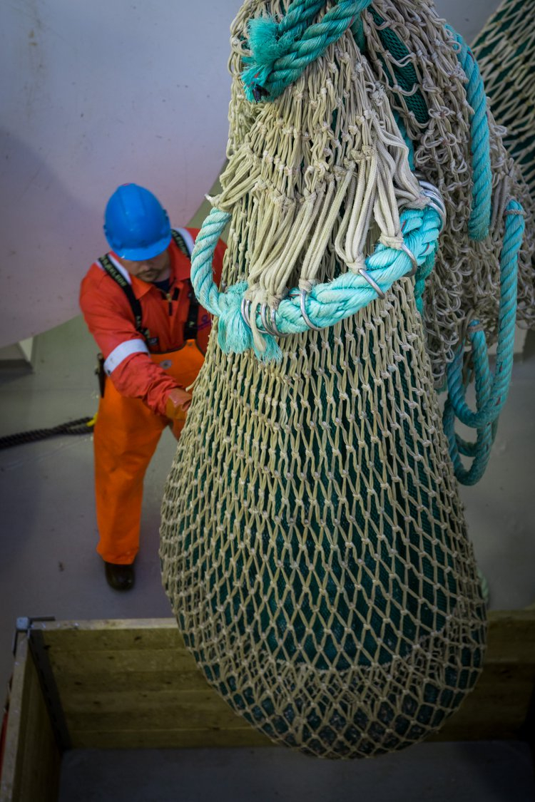A fisherman supporting a fishing net hanging over a wooden container.