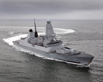 A grey naval vessel making a sharp turn at sea, leaving a circular wake pattern behind under an overcast sky.