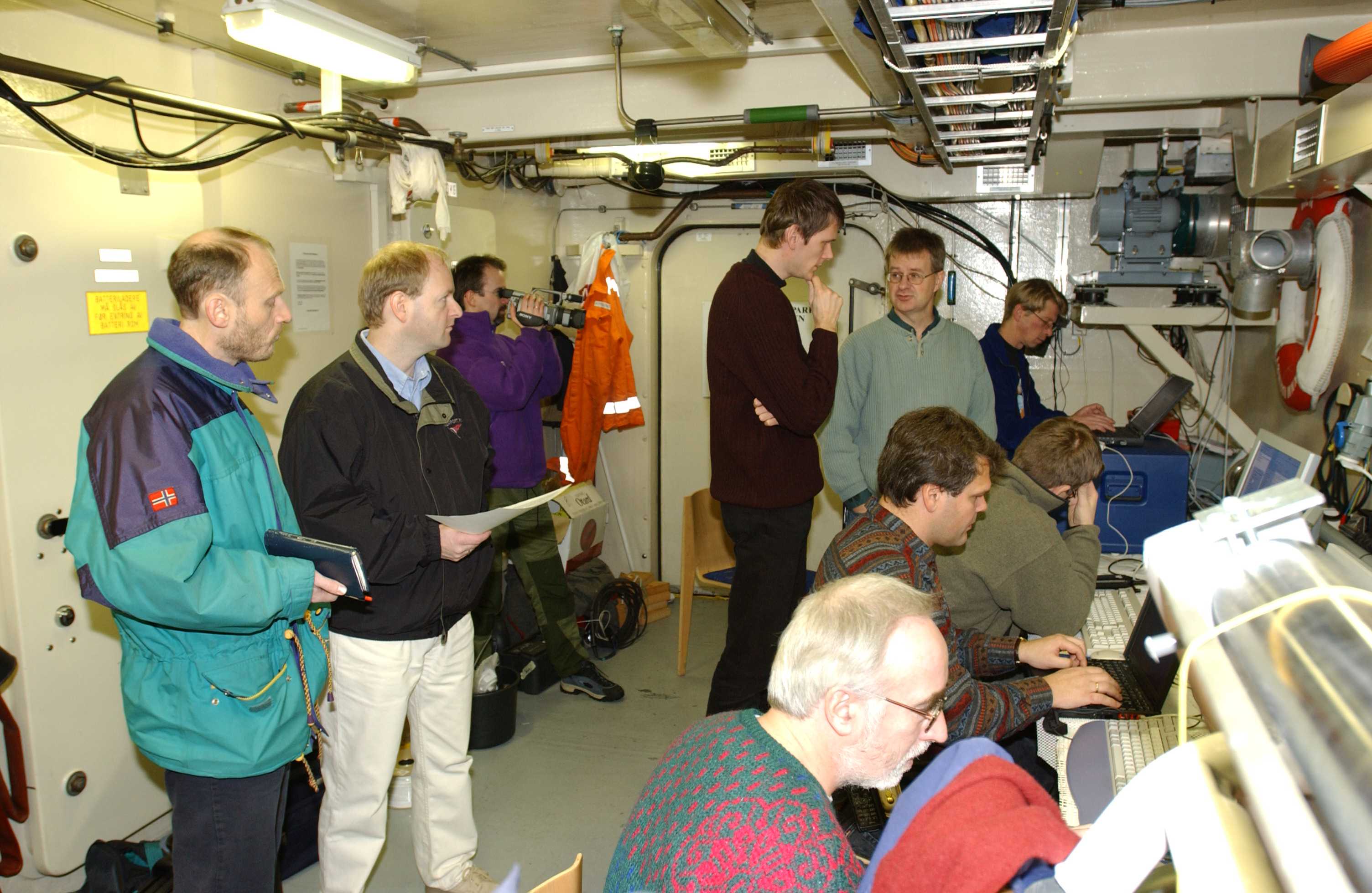 In the ROV hangar onboard the Royal Norwegian Navy mine hunter HNoMS Karmoy during the first full-scale Mine Counter Measure demo in December 2001. Nils Størkersen and Per Espen Hagen standing in the back, on left. Other people pictured are Jan Olav Langseth, Bjørn Hugsted, Petter Lågstad, Bjørn Jalving, Øivind Midtgaard, Jon Kristensen (standing in with pale green top and glasses) and Magne Mandt.