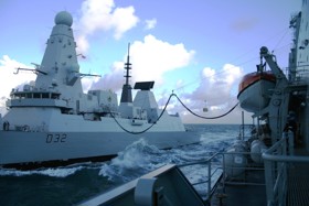 Two naval vessels side by side at sea using the replenishment at sea technology.
