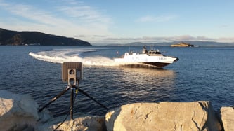 The MBR 189 mounted on a tripod by the sea, with a boat driving by.